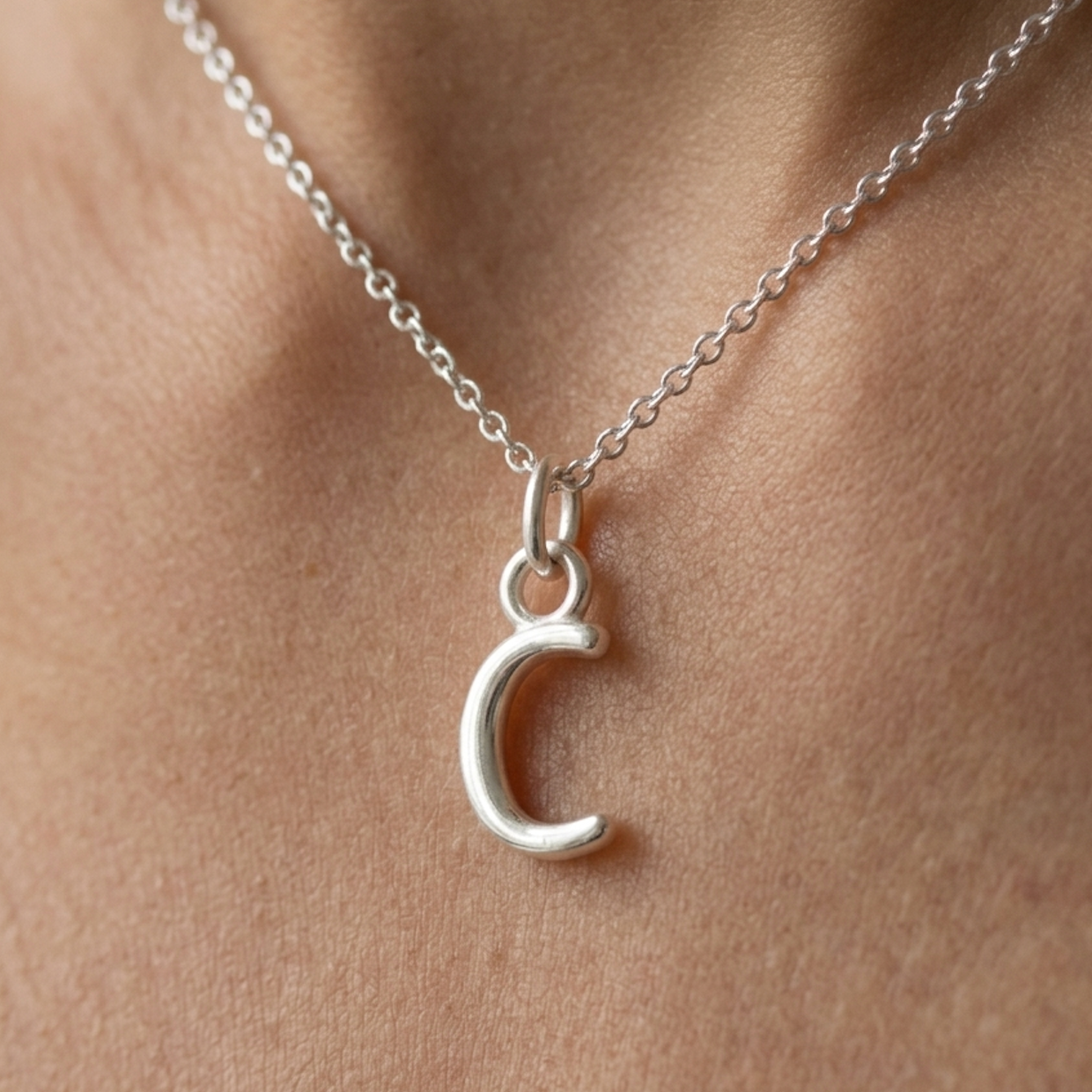 Silver necklace with a C pendant on a person's neck.