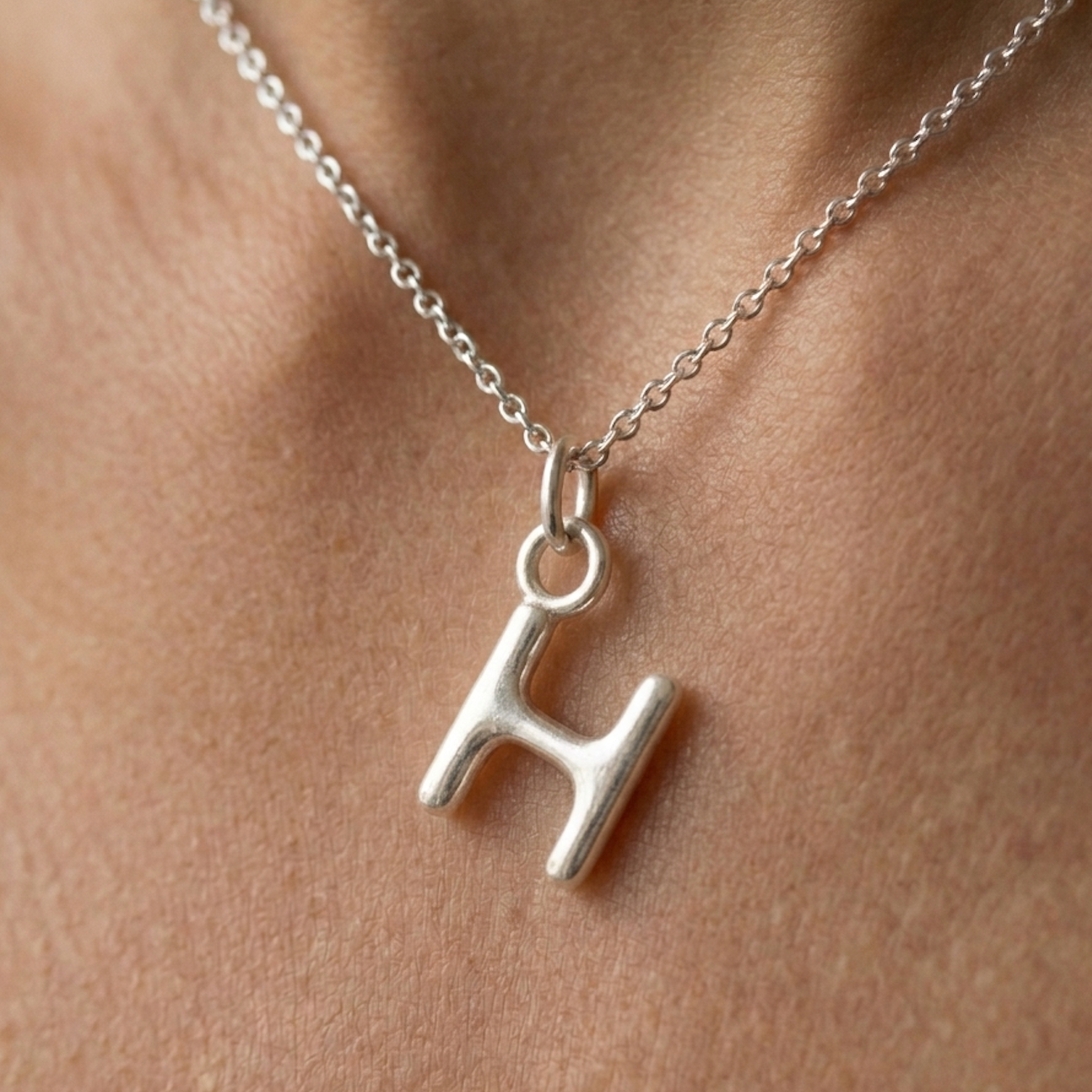 Silver necklace with a 'H' pendant on a person's neck