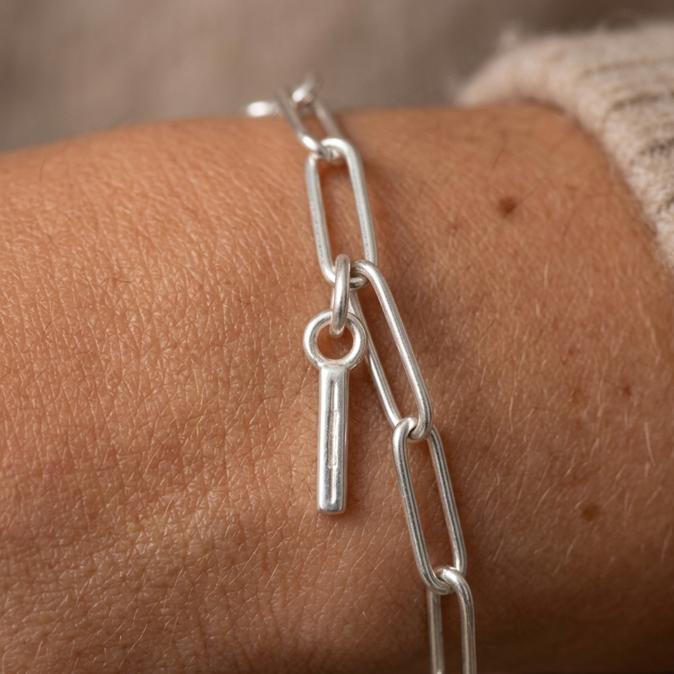 Silver chain bracelet with a I charm on a wrist.