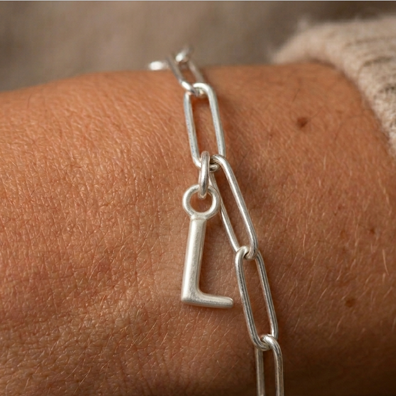 Silver chain bracelet with a letter 'L' charm on a wrist.