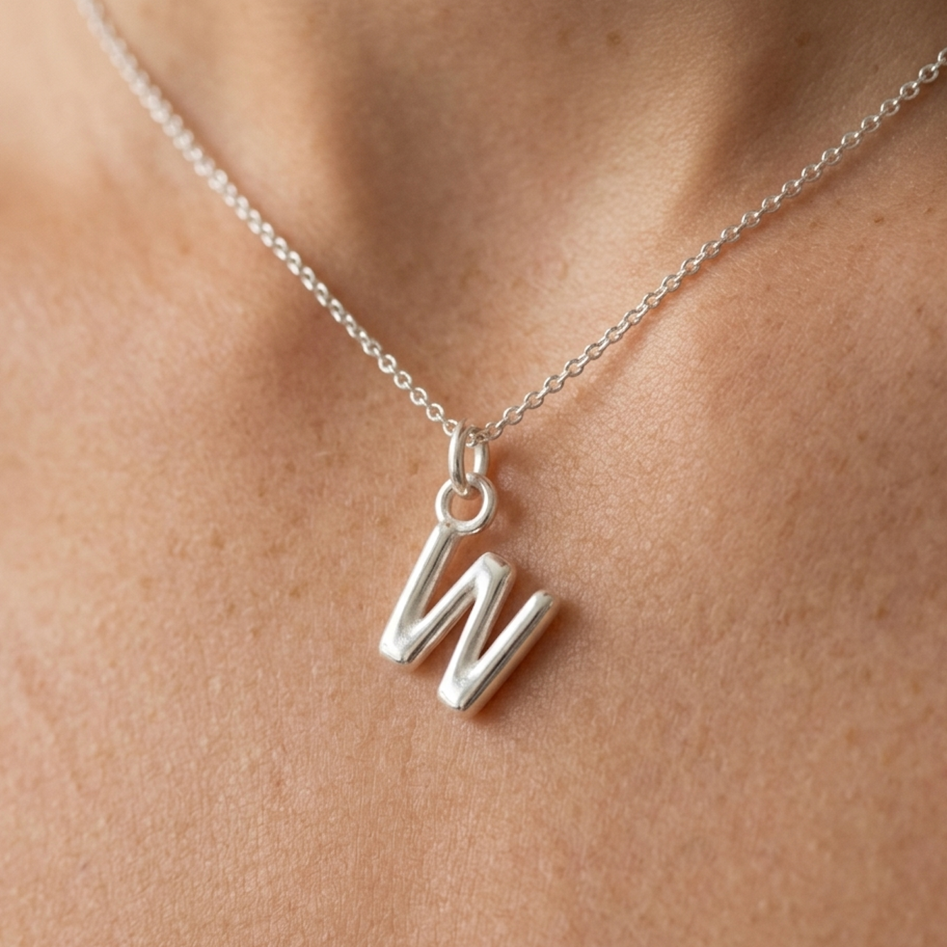 Silver necklace with a 'W' pendant on a person's neck