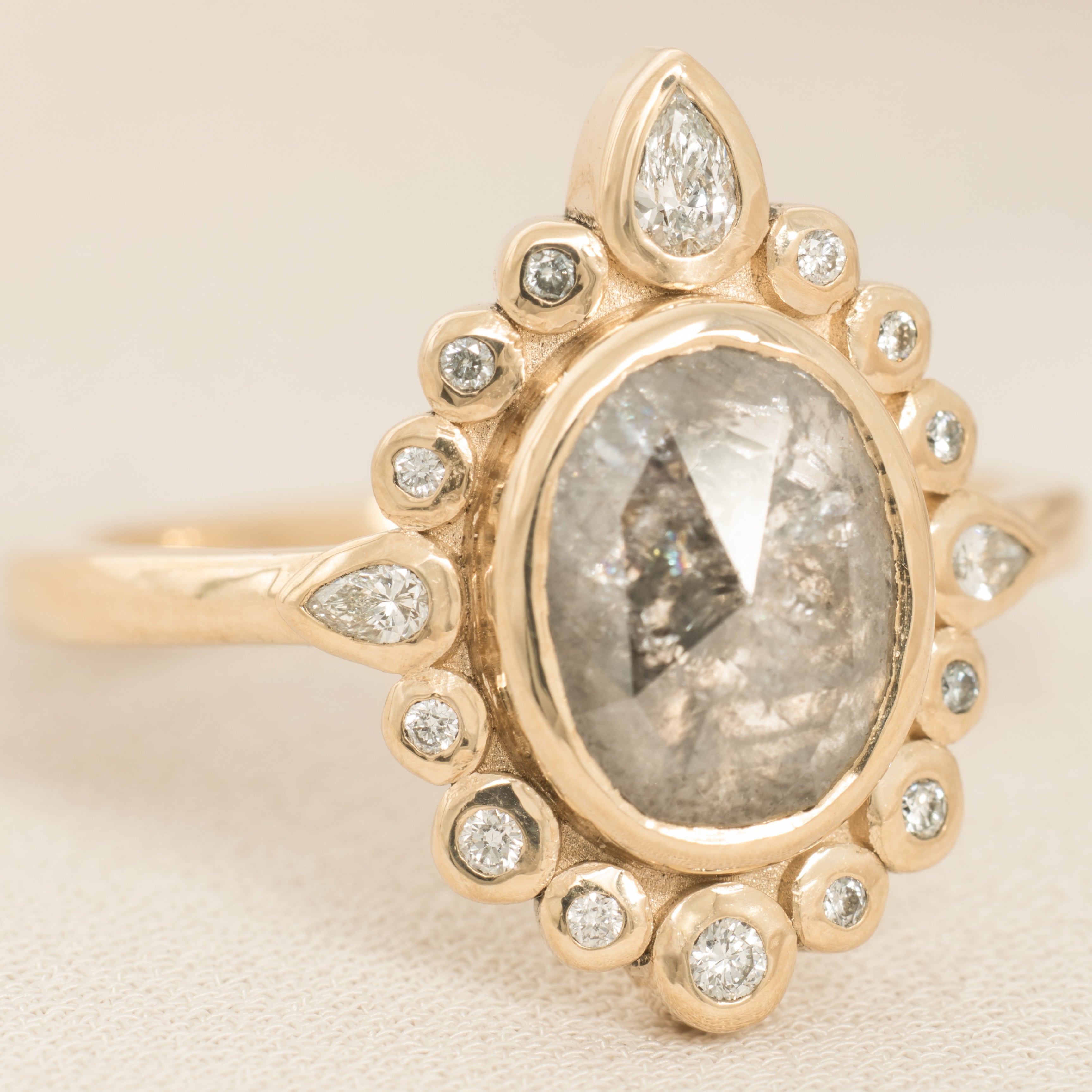 Gold ring with a central salt and pepper diamond and smaller diamonds on a beige background