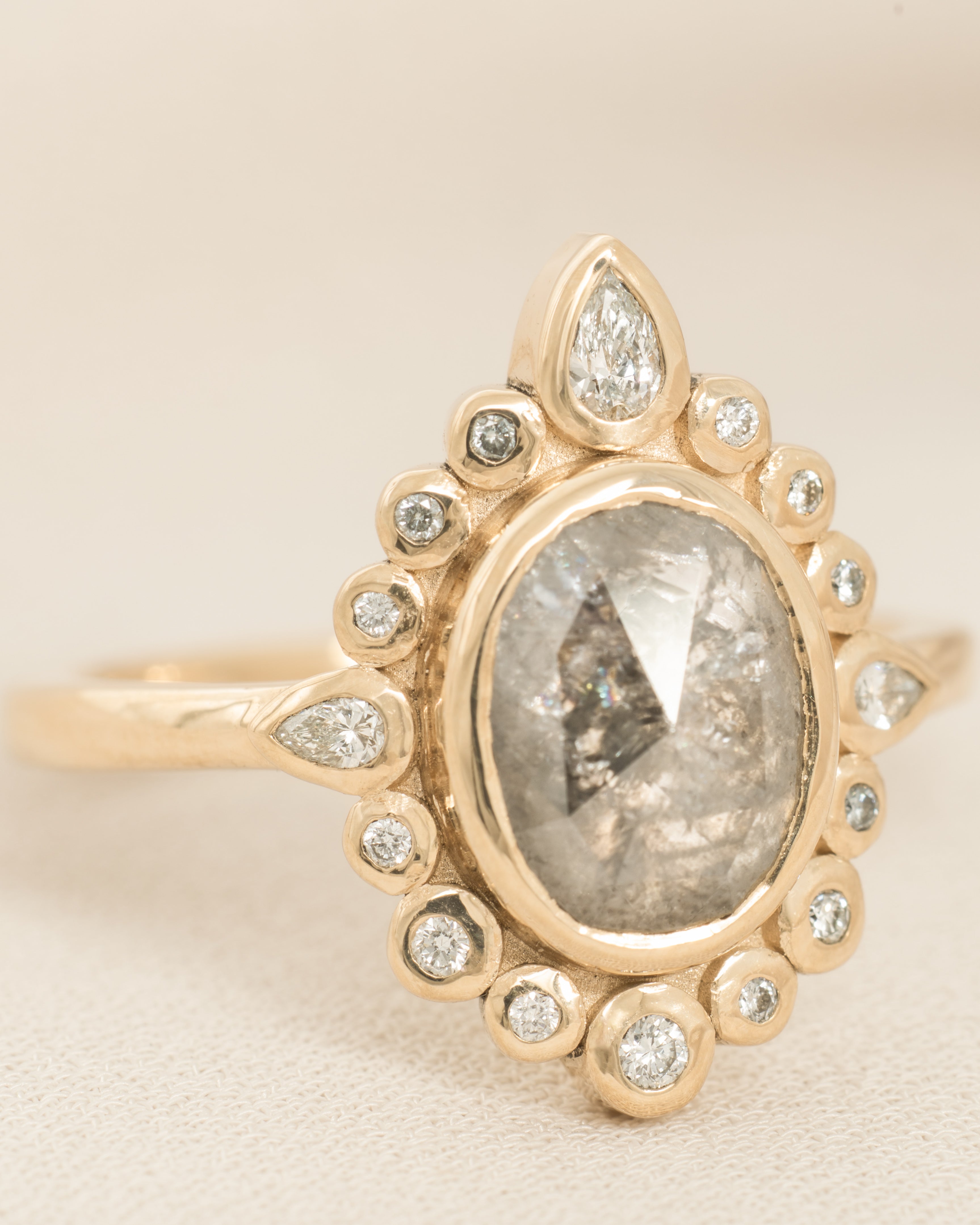 Gold ring with a central salt and pepper diamond and smaller diamonds on a beige background