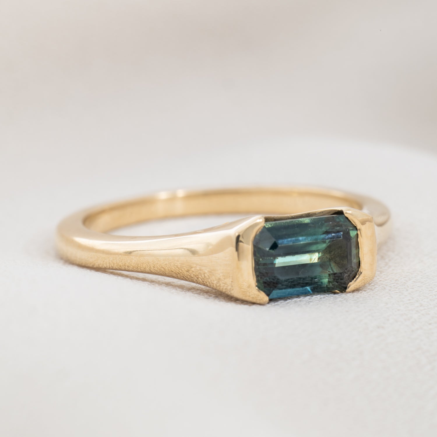 Gold ring with a green gemstone on a light gray background