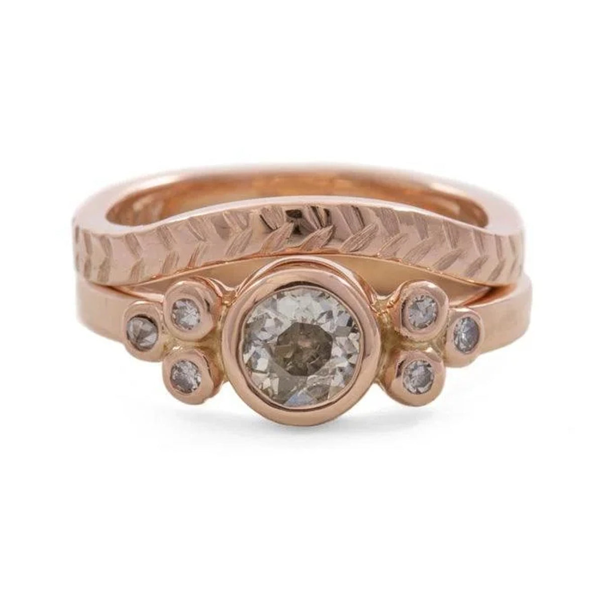 Gala rose-toned engagement ring with a round centre stone and four accent stones, stacked with a chevron band