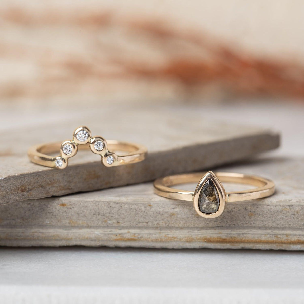 Peri pear salt and pepper diamond ring beside a gold crown band of five white stones on slate