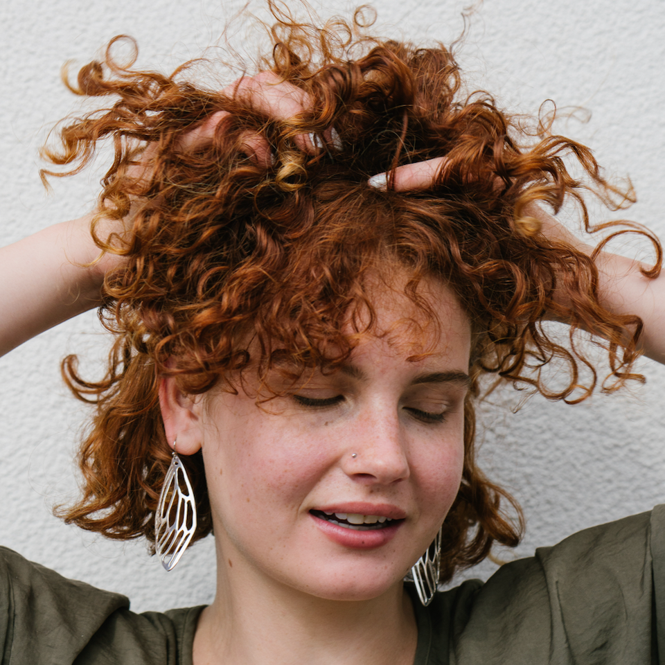 Model with curly red hair wearing large sterling silver cicada wing earrings