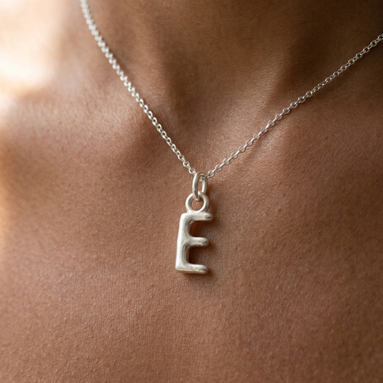 Silver necklace with a letter 'E' pendant on a person's neck