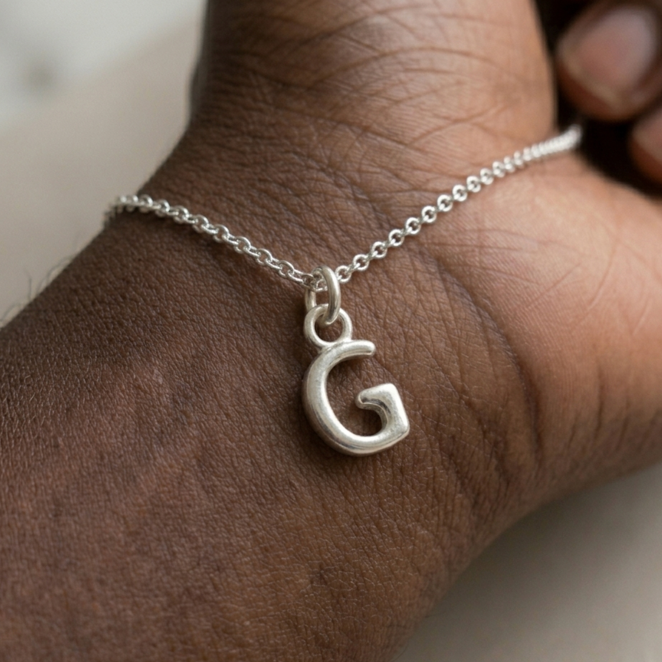 Silver bracelet with a 'G' charm on a wrist.