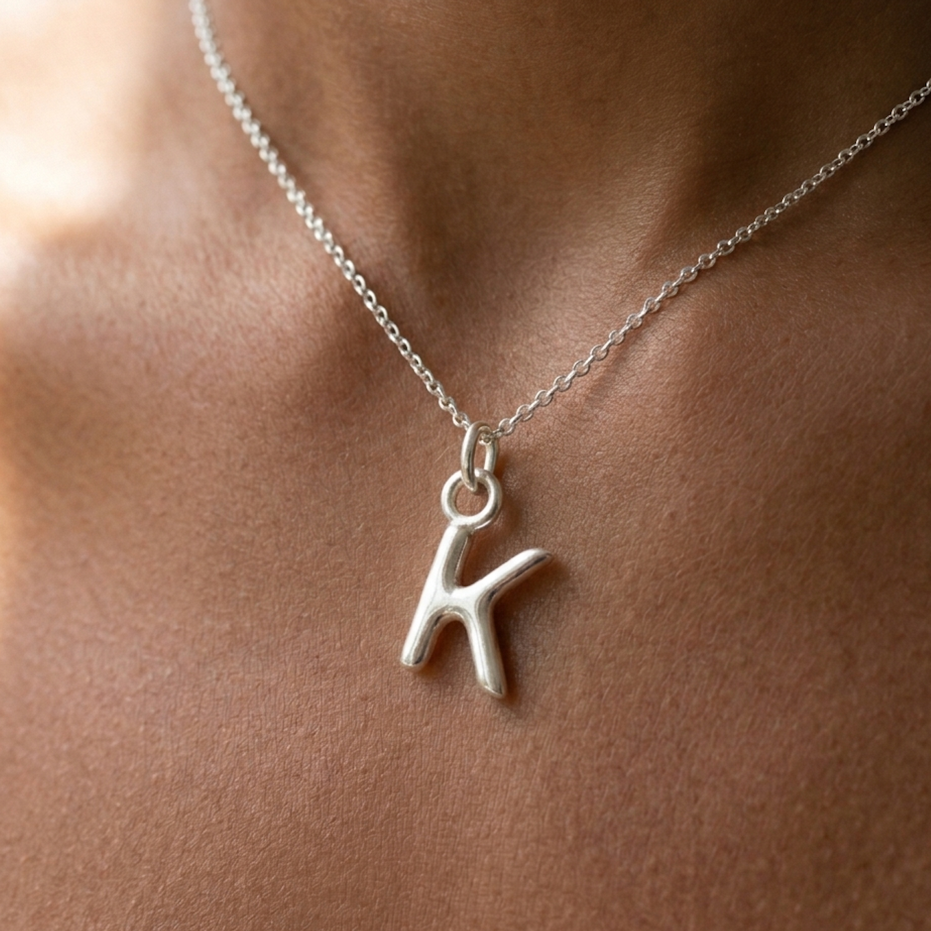 Silver necklace with a 'K' pendant on a person's neck