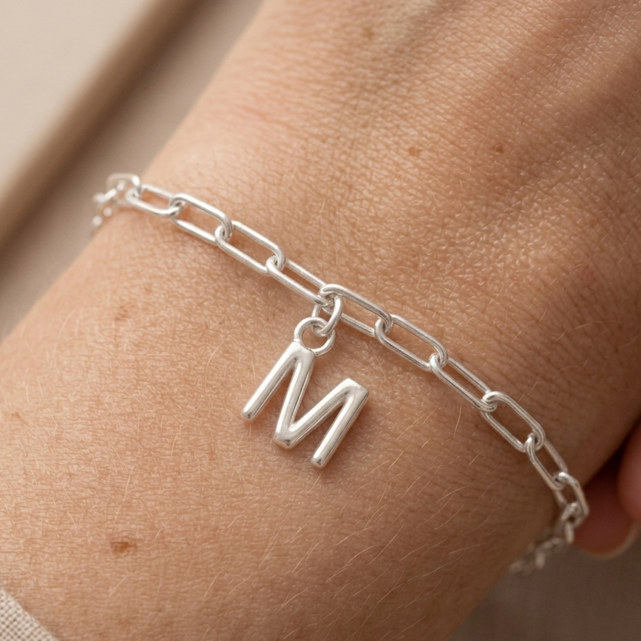 Silver chain bracelet with a 'M' charm on a wrist.