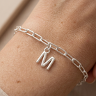 Silver chain bracelet with a 'M' charm on a wrist.