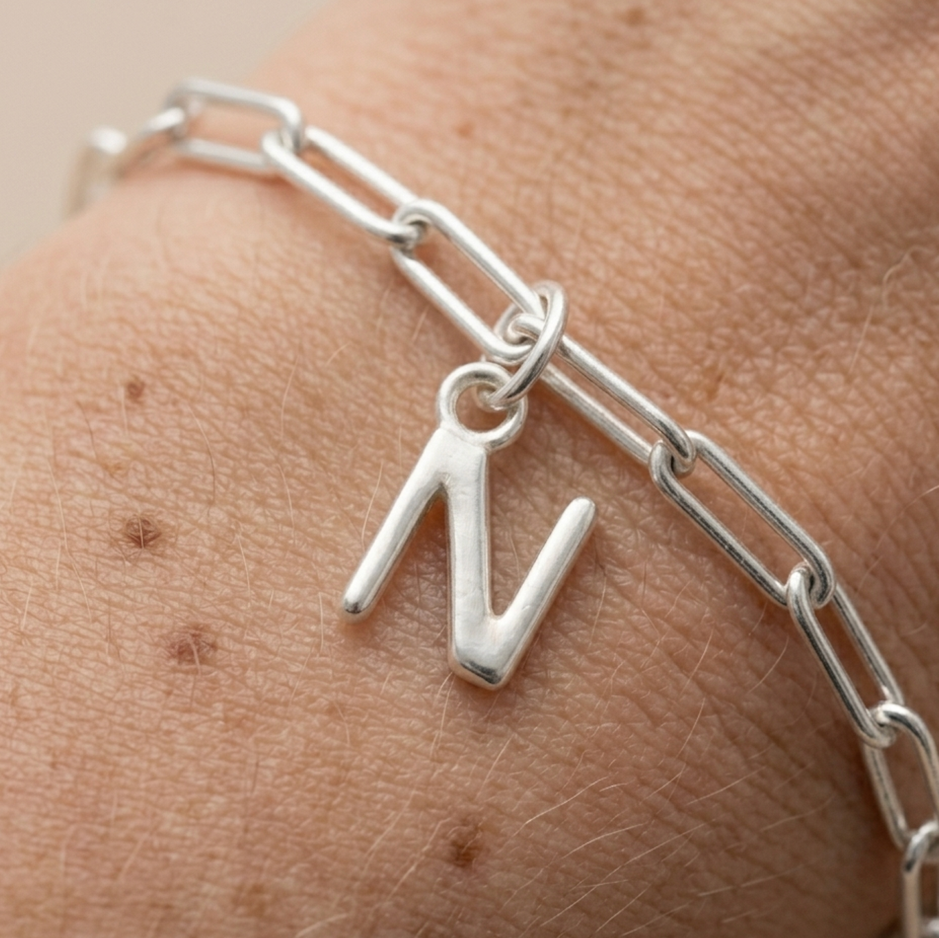 Silver chain bracelet with a 'N' charm on a wrist.