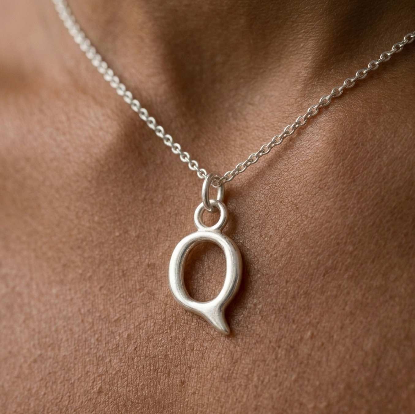 Silver necklace with a Q pendant on a person's neck
