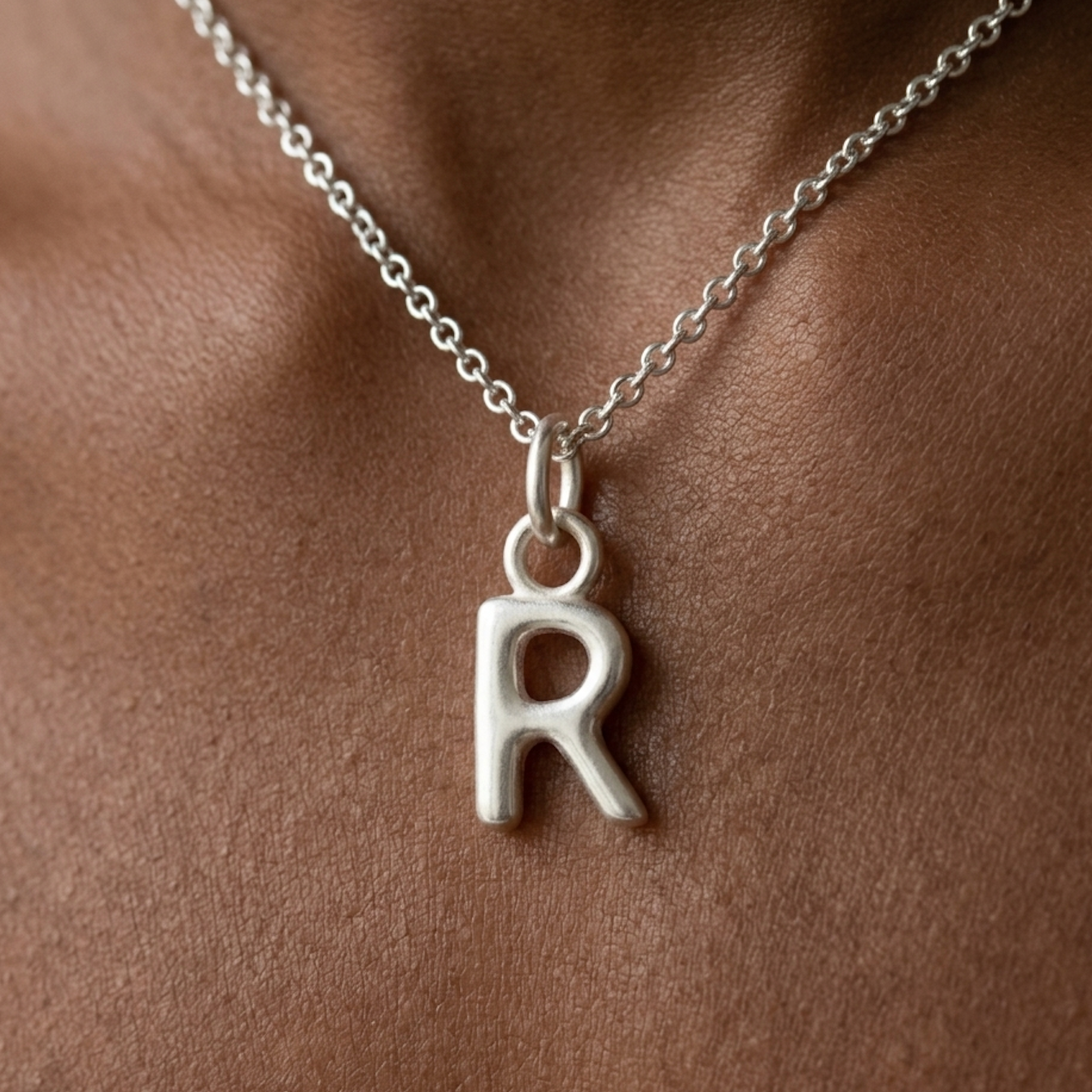 Silver necklace with a 'R' pendant on a persons neck