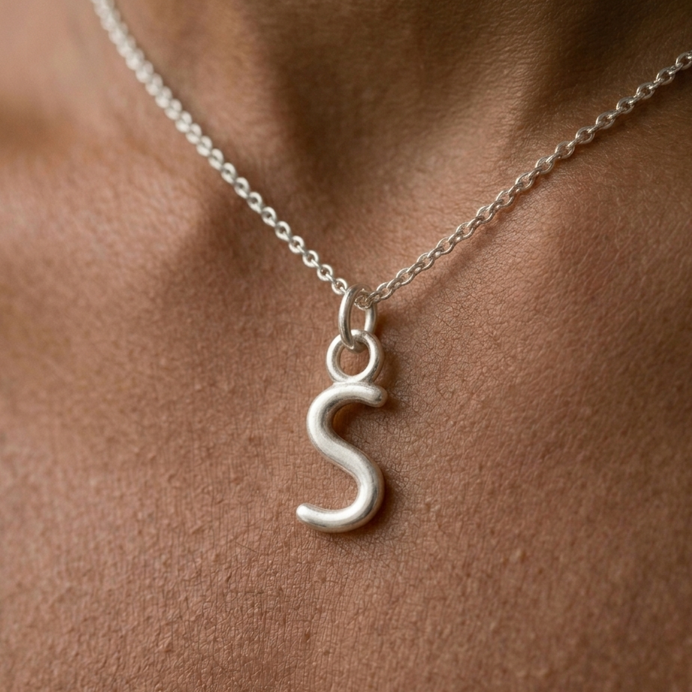 Silver necklace with a 'S' pendant on a person's neck