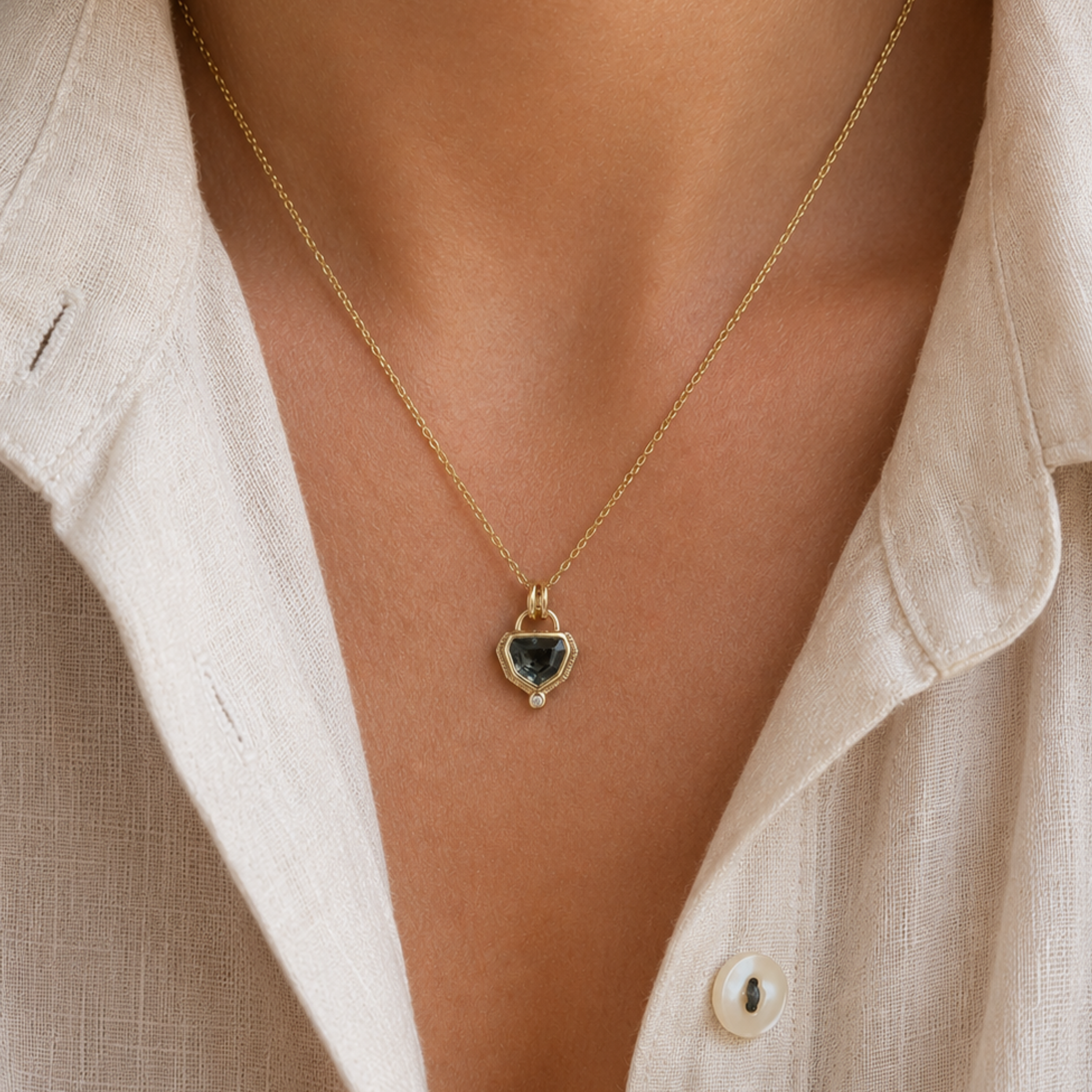 Shield shaped Pendant styled on Gold necklace on a person wearing a beige shirt.