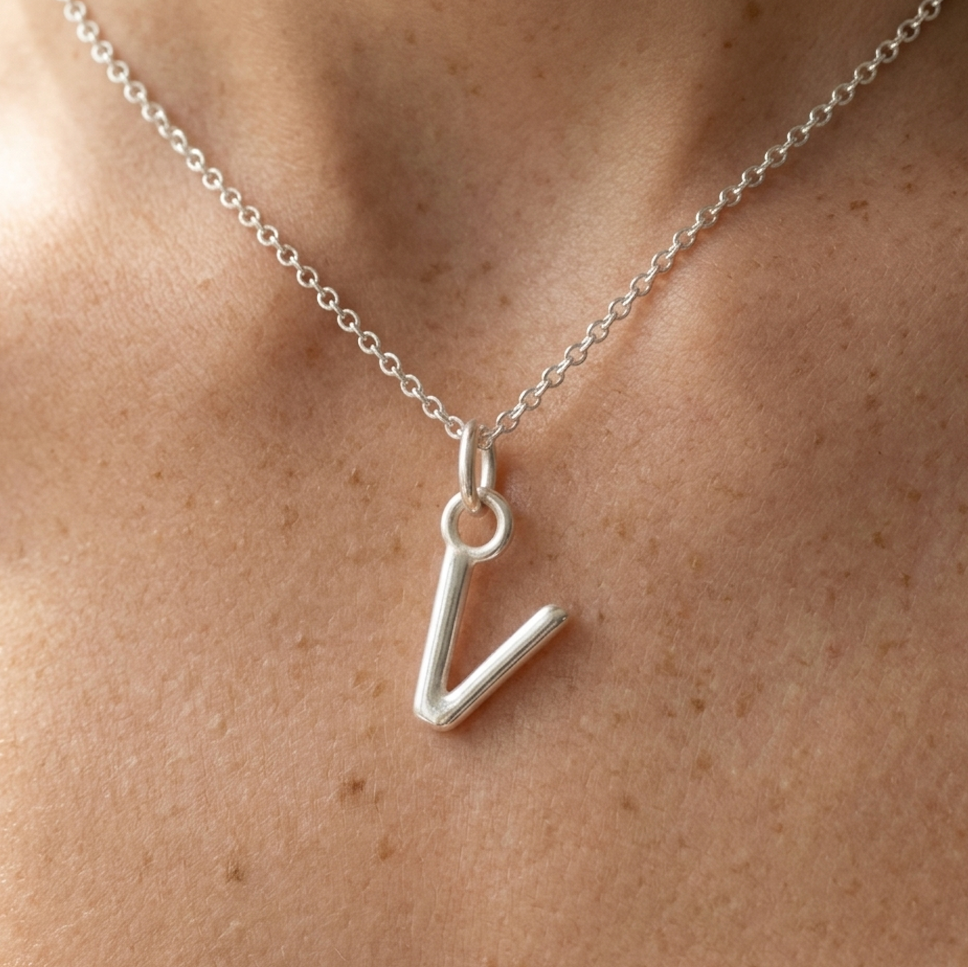 Silver necklace with a 'V' pendant on a person's neck