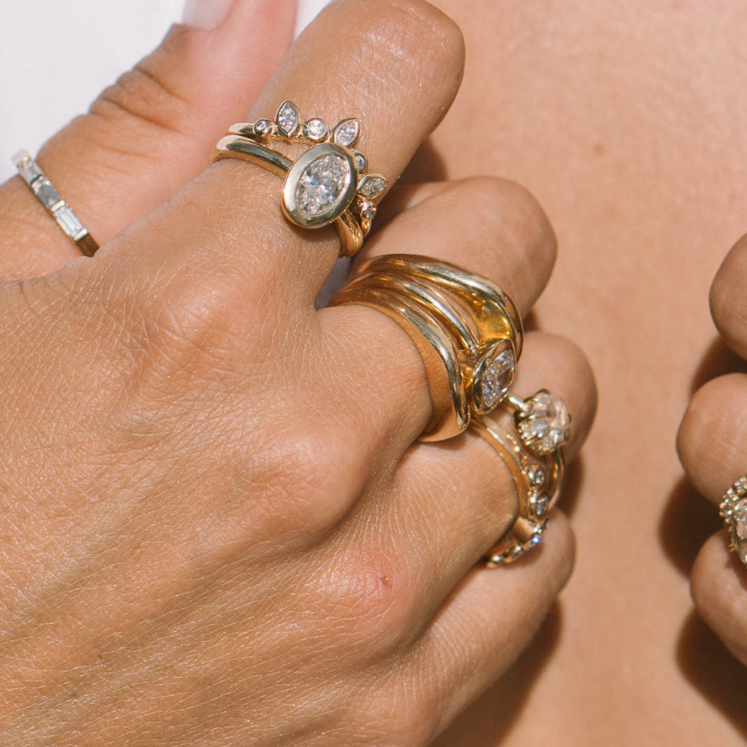 Close-up of a person's hands wearing multiple gold and silver rings with clear gemstones, styled over a white top.