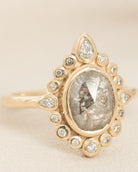 Gold ring with a central salt and pepper diamond and smaller diamonds on a beige background