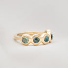 Gold ring with green gemstones on a light gray background