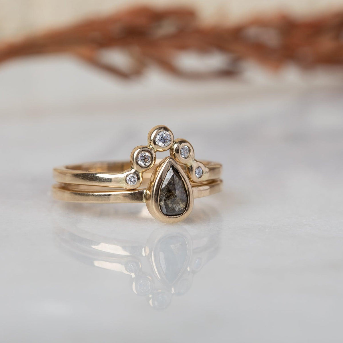 Peri pear salt and pepper diamond ring stacked with a gold crown band of five white stones on marble
