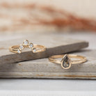 Peri pear salt and pepper diamond ring beside a gold crown band of five white stones on slate